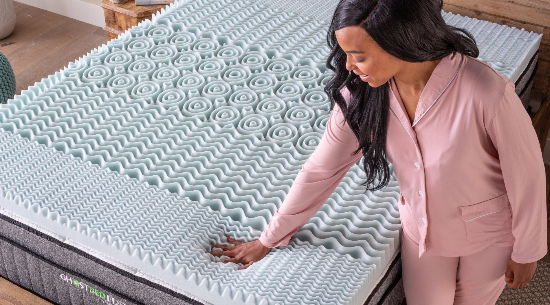 A young woman places a memory foam mattress topper on her bed.